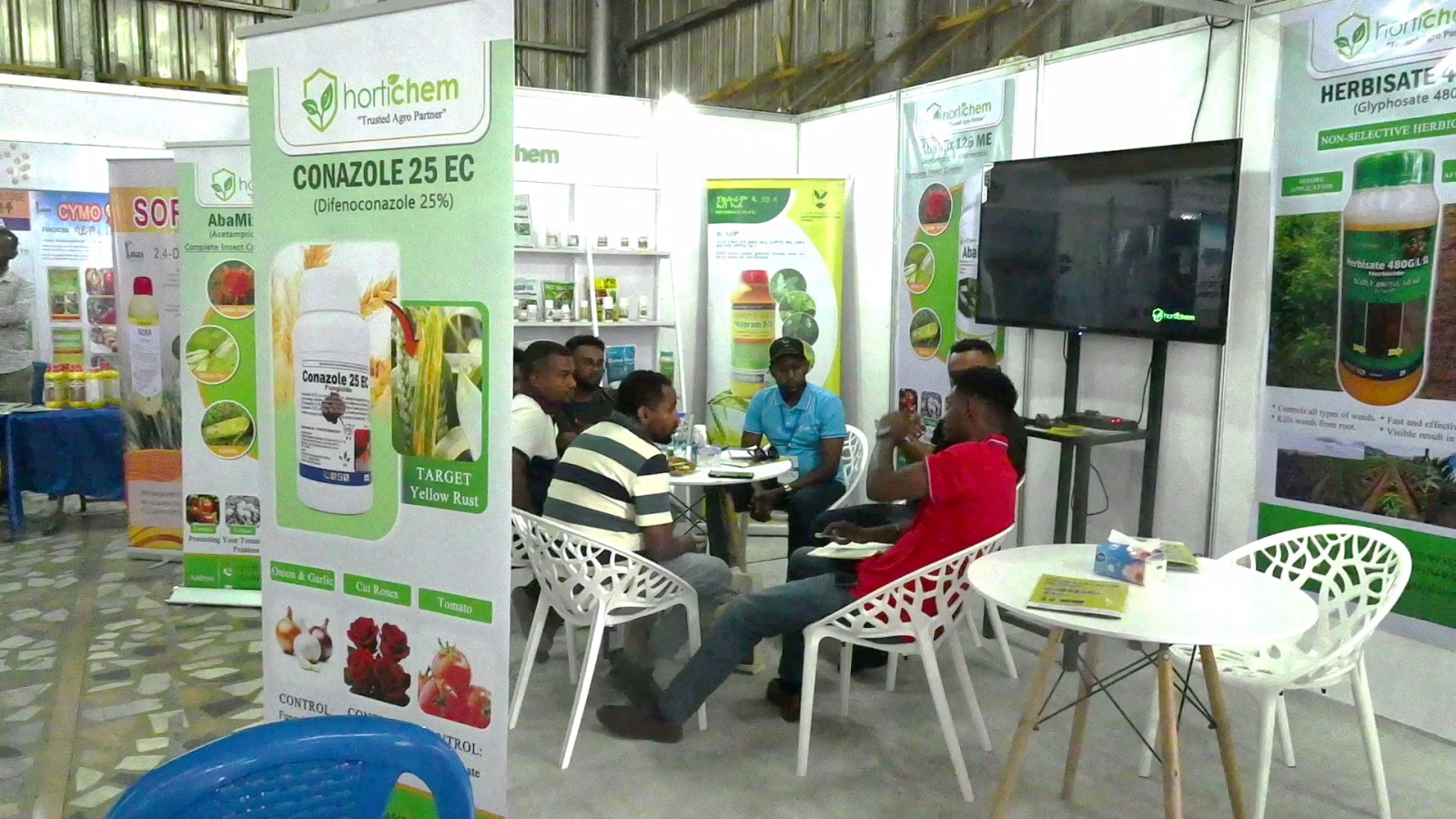 An input supplier stand displaying crop protection products, with visitors seated alongside.